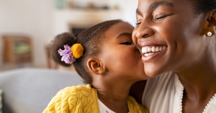 Young Black child kissing smiling mother on the cheek Credit: Ground Picture/Shutterstock